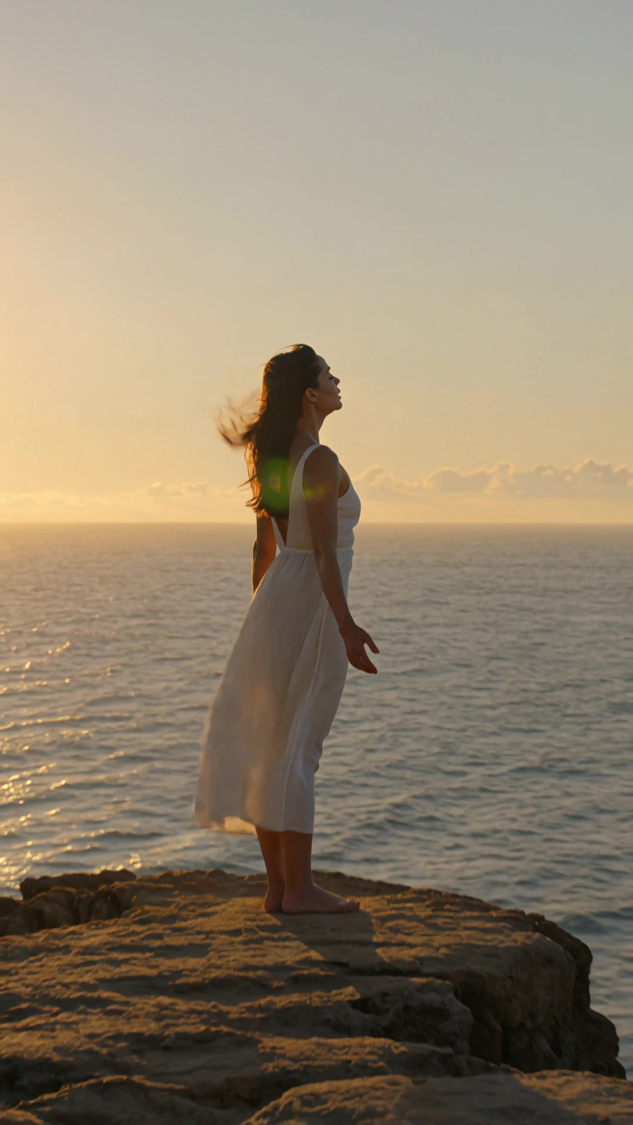 Woman on clifftop at golden hour with arms open